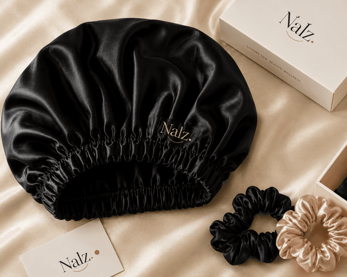 Nalz noir silk bonnet with gold embroidered wordmark, styled with scrunchies and packaging